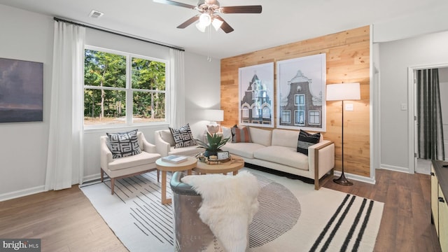 living room featuring ceiling fan, wood walls, and dark hardwood / wood-style floors