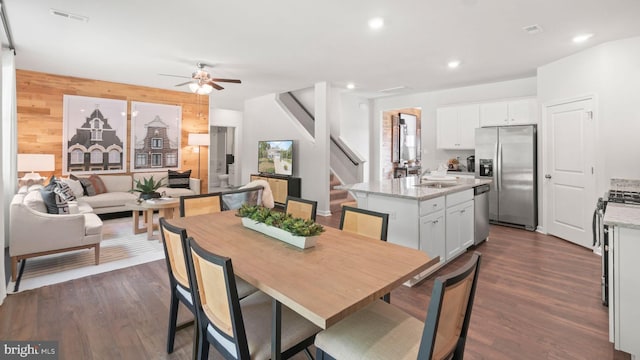 dining space with dark hardwood / wood-style flooring, wooden walls, ceiling fan, and sink