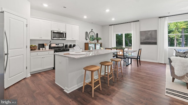 kitchen featuring a center island with sink, white cabinetry, light stone countertops, and dark wood-type flooring