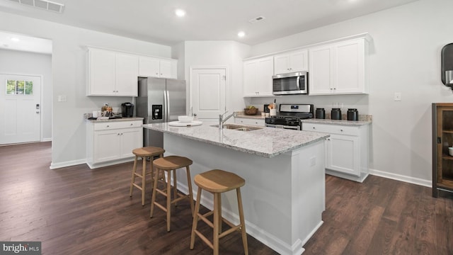 kitchen with dark hardwood / wood-style flooring, white cabinets, appliances with stainless steel finishes, and an island with sink