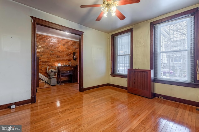 unfurnished room with brick wall, a healthy amount of sunlight, ceiling fan, and light hardwood / wood-style flooring