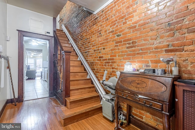 stairway featuring brick wall, ceiling fan, and light hardwood / wood-style flooring