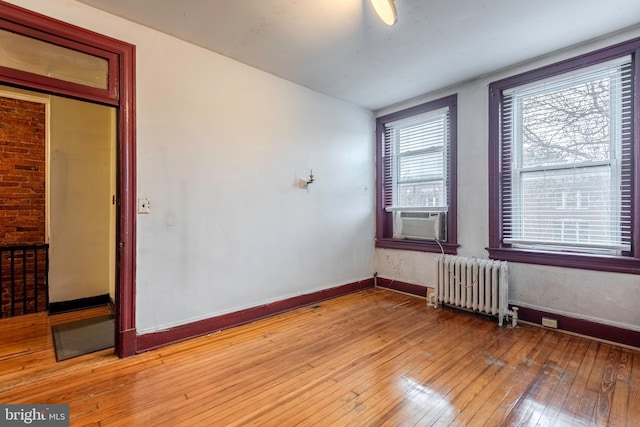 empty room with brick wall, light wood-type flooring, and radiator