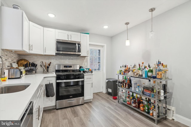 kitchen featuring decorative light fixtures, appliances with stainless steel finishes, tasteful backsplash, white cabinets, and light wood-type flooring