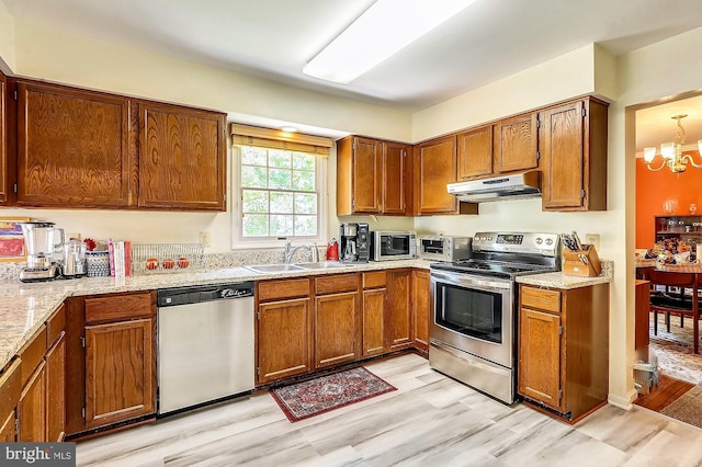 kitchen featuring sink, light stone counters, an inviting chandelier, light hardwood / wood-style flooring, and stainless steel appliances