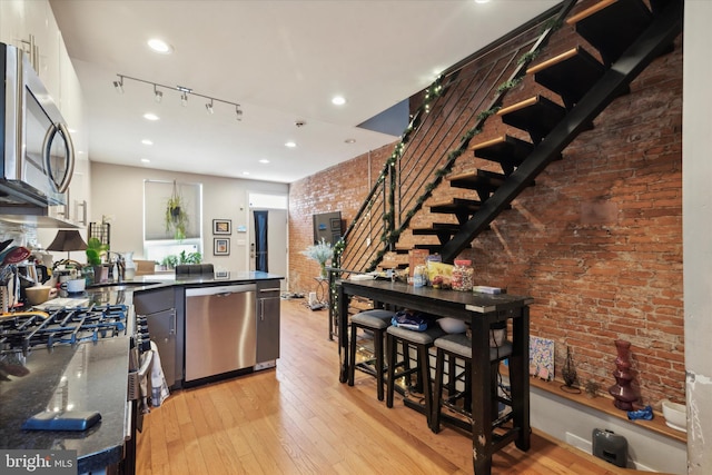 kitchen featuring rail lighting, light hardwood / wood-style floors, white cabinetry, stainless steel appliances, and brick wall