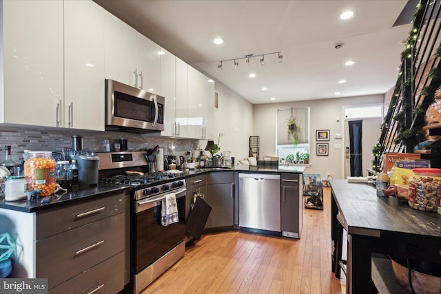 kitchen with white cabinetry, backsplash, kitchen peninsula, track lighting, and appliances with stainless steel finishes