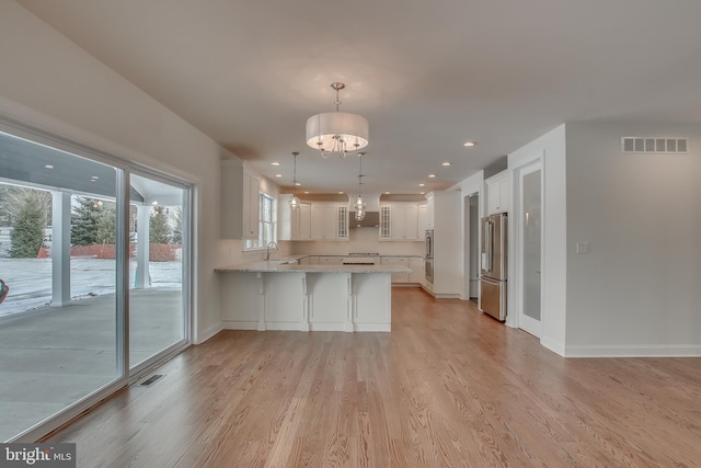 kitchen featuring a notable chandelier, decorative light fixtures, appliances with stainless steel finishes, white cabinetry, and light wood-type flooring