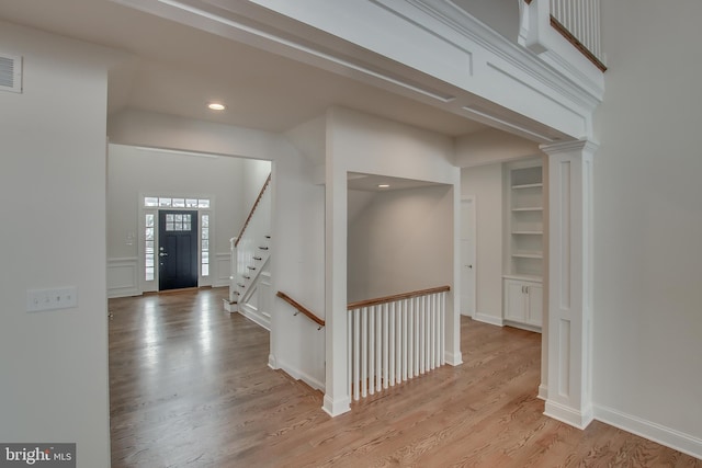 hallway featuring built in shelves, light hardwood / wood-style flooring, and ornate columns