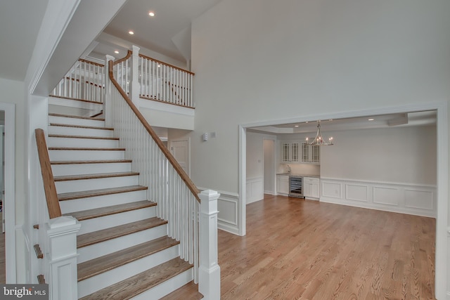 staircase featuring a high ceiling, beverage cooler, a chandelier, and light hardwood / wood-style flooring