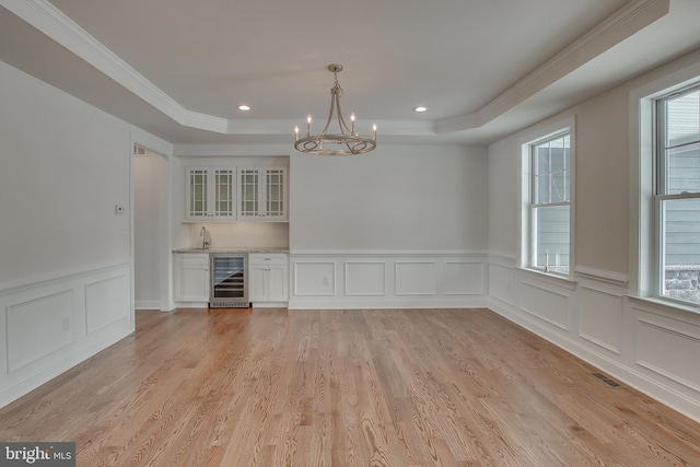 empty room featuring a raised ceiling, light hardwood / wood-style floors, and beverage cooler