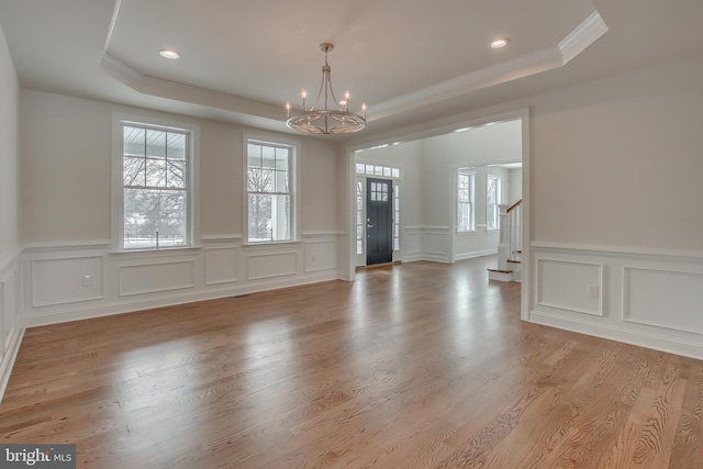 empty room with a chandelier, light hardwood / wood-style floors, crown molding, and a tray ceiling