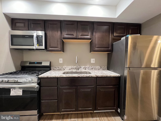 kitchen featuring light stone countertops, appliances with stainless steel finishes, dark hardwood / wood-style flooring, dark brown cabinets, and sink