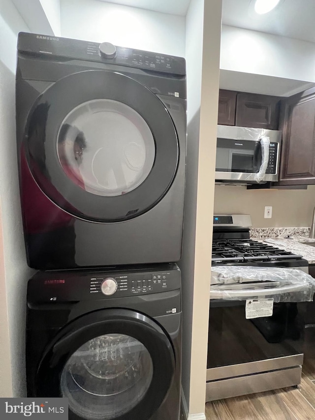 clothes washing area featuring stacked washing maching and dryer and light hardwood / wood-style floors