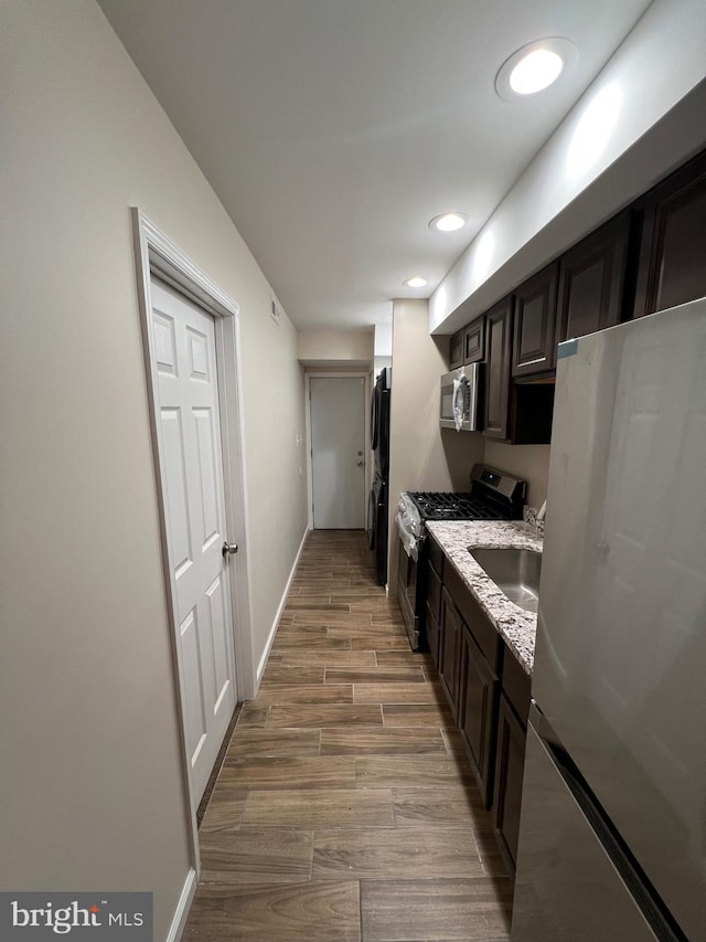 kitchen with light stone countertops, appliances with stainless steel finishes, dark brown cabinetry, sink, and light hardwood / wood-style flooring