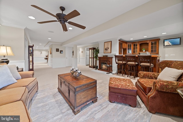 living room with a fireplace, ceiling fan, bar, ornamental molding, and light carpet