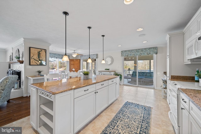 kitchen with ceiling fan, a kitchen island, hanging light fixtures, a fireplace, and white cabinetry