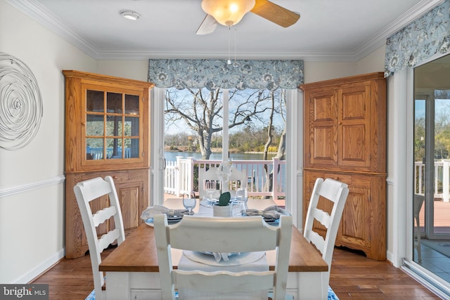 dining area with a water view, dark wood-type flooring, ceiling fan, and crown molding