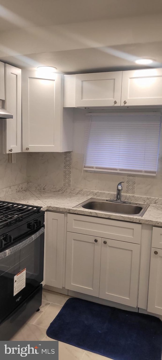 kitchen with light stone countertops, black range with gas cooktop, tasteful backsplash, white cabinets, and sink