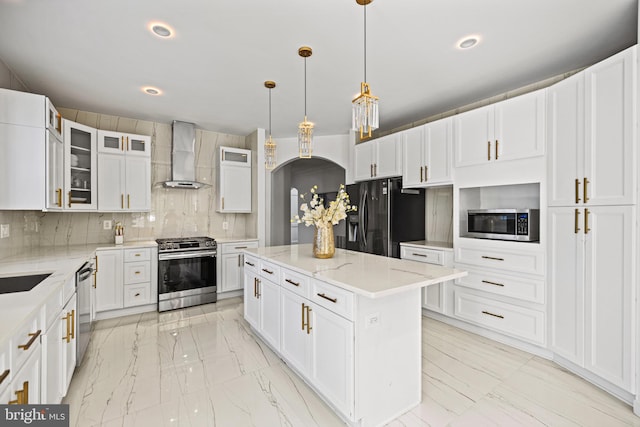 kitchen with wall chimney range hood, tasteful backsplash, hanging light fixtures, a kitchen island, and appliances with stainless steel finishes