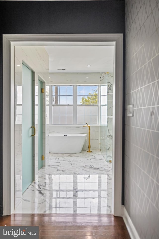 bathroom featuring a bath, hardwood / wood-style flooring, and tile walls