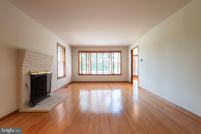 unfurnished living room featuring brick wall, a wood stove, and light hardwood / wood-style flooring