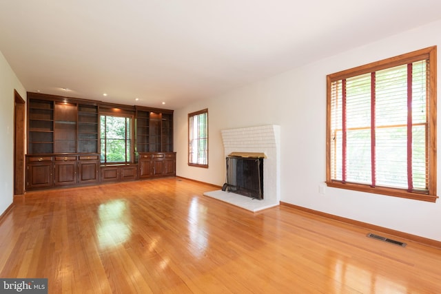 unfurnished living room featuring light hardwood / wood-style flooring, built in shelves, and a brick fireplace