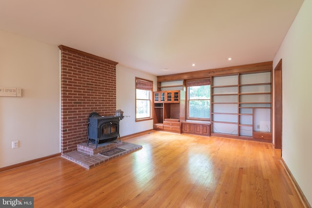 unfurnished living room with light hardwood / wood-style floors, a wood stove, and brick wall