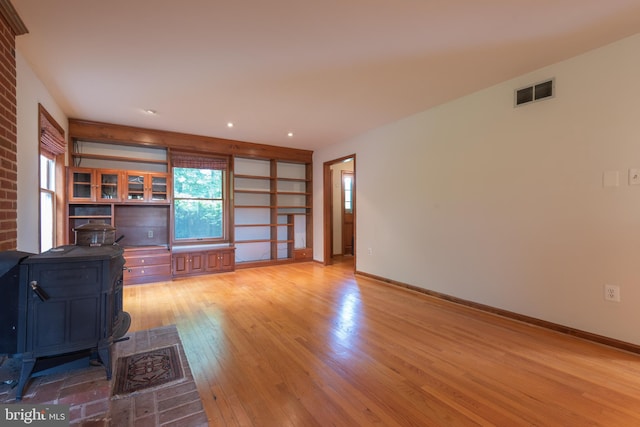 unfurnished living room with brick wall, a wood stove, and light hardwood / wood-style floors