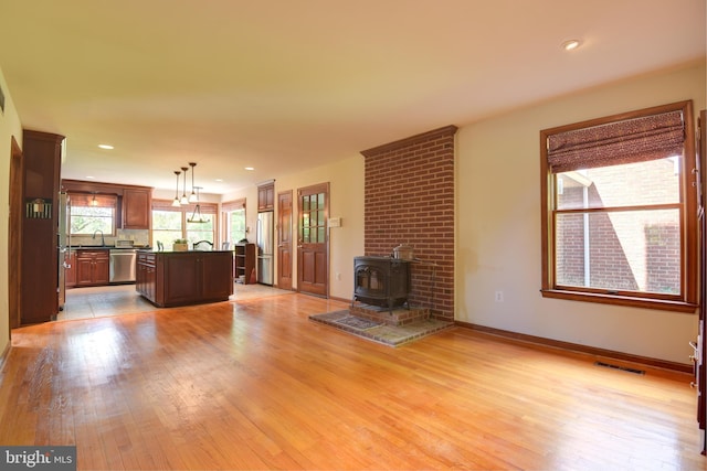 unfurnished living room with sink, light hardwood / wood-style floors, a wood stove, and brick wall