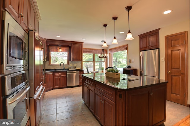 kitchen with plenty of natural light, pendant lighting, backsplash, a kitchen island, and appliances with stainless steel finishes