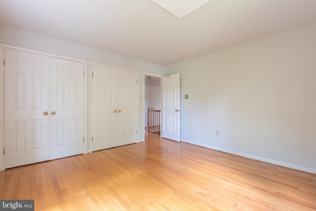 unfurnished bedroom featuring multiple closets and light wood-type flooring