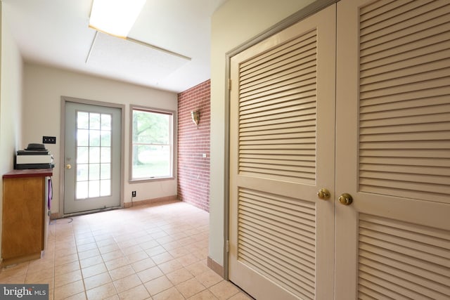 corridor featuring light tile flooring and brick wall