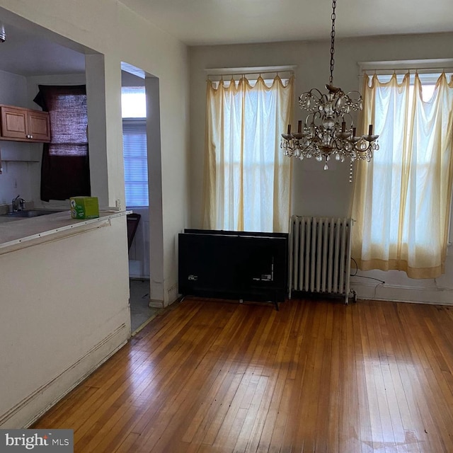 unfurnished dining area featuring an inviting chandelier, radiator, sink, and hardwood / wood-style flooring