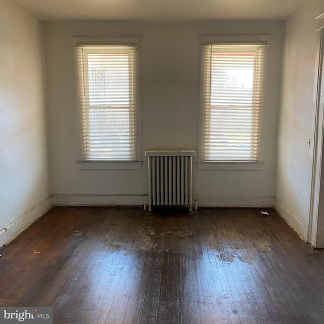 unfurnished room with dark hardwood / wood-style flooring, plenty of natural light, and radiator