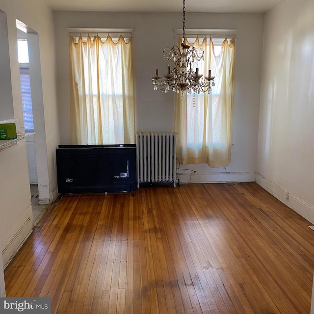 empty room with an inviting chandelier, radiator, and dark hardwood / wood-style floors