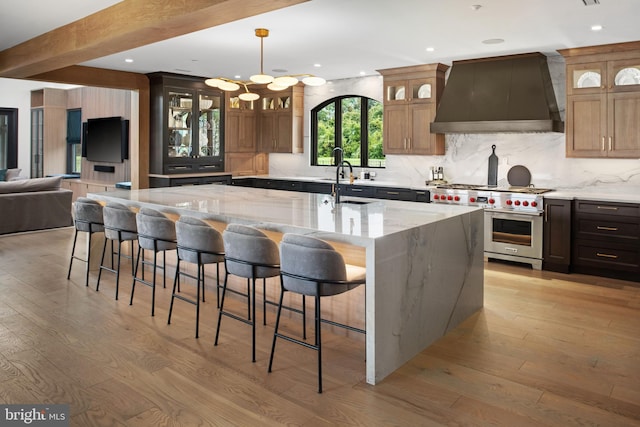 kitchen featuring a kitchen breakfast bar, light hardwood / wood-style flooring, wall chimney range hood, and an island with sink