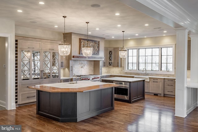 kitchen with tasteful backsplash, dark hardwood / wood-style floors, a kitchen island with sink, sink, and decorative columns