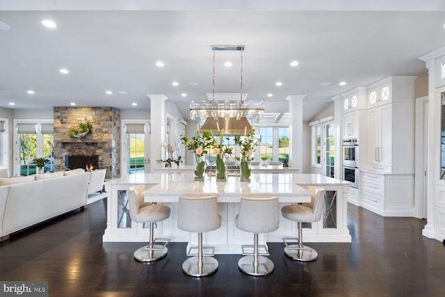 kitchen with white cabinets, pendant lighting, a stone fireplace, and dark wood-type flooring