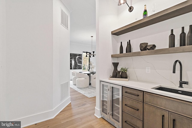 bar with light stone countertops, beverage cooler, sink, pendant lighting, and light hardwood / wood-style flooring