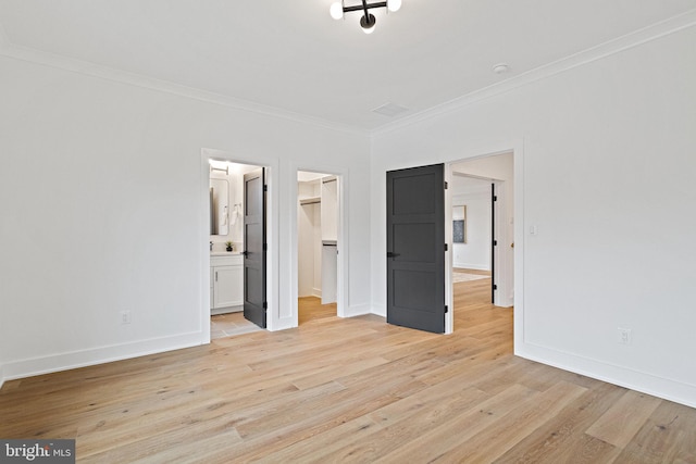 unfurnished bedroom with a spacious closet, ensuite bathroom, light wood-type flooring, and crown molding