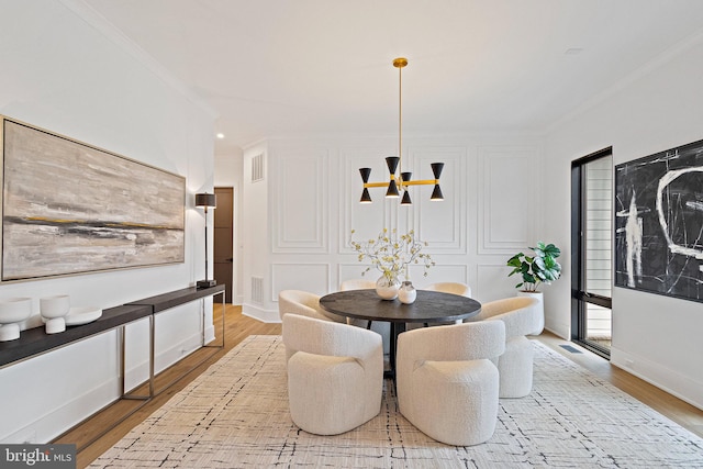 dining space with light wood-type flooring, ornamental molding, and an inviting chandelier