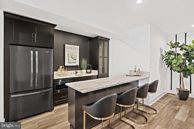 bar featuring light stone counters, light hardwood / wood-style flooring, stainless steel appliances, and sink