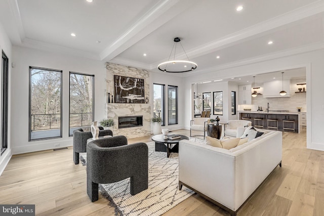 living room with beamed ceiling, crown molding, light wood-type flooring, and a fireplace