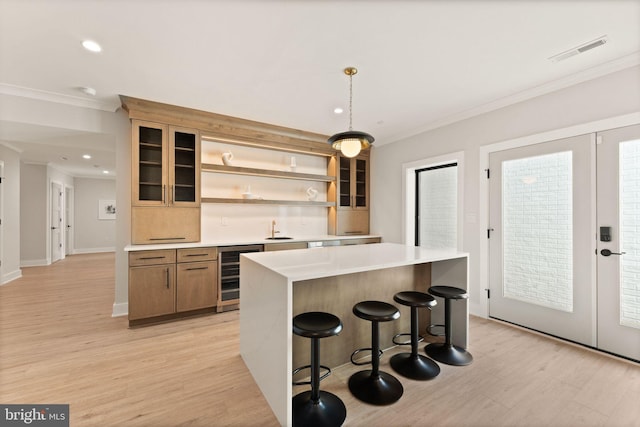 kitchen with sink, beverage cooler, light hardwood / wood-style flooring, pendant lighting, and a kitchen bar