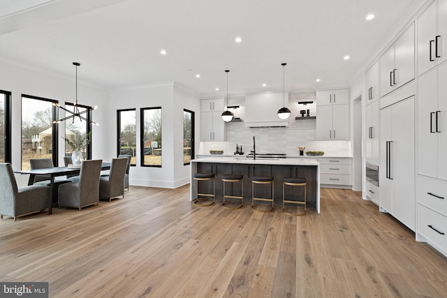 kitchen with a kitchen bar, backsplash, light hardwood / wood-style flooring, white cabinets, and an island with sink