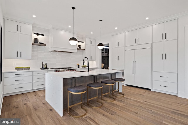 kitchen featuring paneled refrigerator, decorative backsplash, a center island with sink, white cabinets, and light wood-type flooring