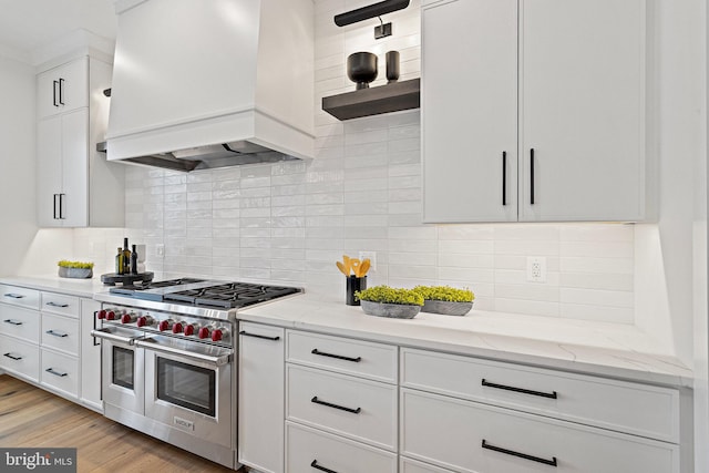 kitchen with premium range hood, range with two ovens, decorative backsplash, light hardwood / wood-style floors, and light stone counters