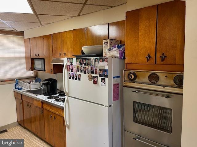 kitchen featuring oven, white fridge, light tile flooring, a paneled ceiling, and gas cooktop