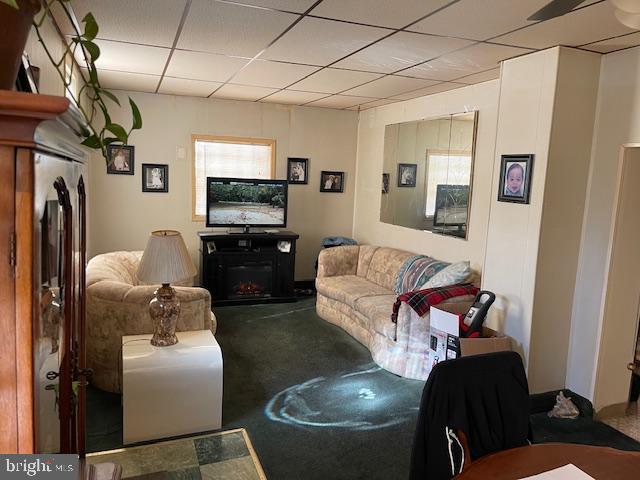 living room with carpet flooring, a drop ceiling, and a fireplace